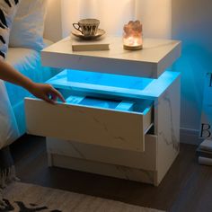 a white table with blue light under it and a person reaching for something in the drawer