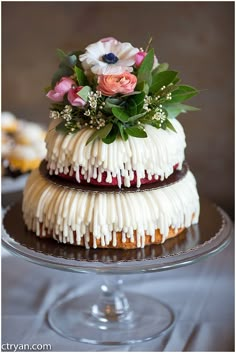 two tiered cake with white icing and flowers on top sitting on a glass plate