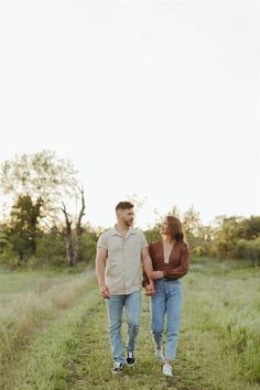 a man and woman holding hands walking down a path in the middle of a field