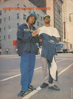 two men standing next to each other in front of a city street with tall buildings