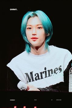 a person with blue hair sitting in front of a tv screen wearing a marine t - shirt