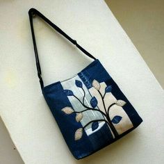 a blue purse with an embroidered tree on the front and side, hanging from a wall