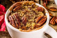 a white mug filled with pecans and crumbs on top of a wooden table