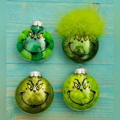 four green ornaments with yellow eyes and grin faces on them, sitting on a blue wooden surface