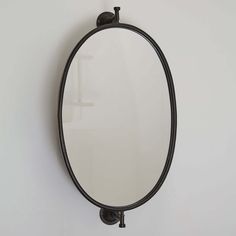 an oval mirror mounted on the wall above a faucet with a black handle