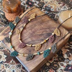 a necklace with beads and leaves is on a wooden table next to a candle,