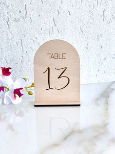 a wooden table number sitting on top of a white counter next to some pink flowers