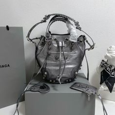 Balenciaga 's popular 'Le Cagole' series is a modern interpretation of its 'City' handbags - reshaped into a bucket bag design to inject a new soul into it. The large size adds two round top handles, combining classic and Modern trends are perfectly integrated. On the basis of retaining the original DNA of the motorcycle bag's flat rivets, delicate buckles and tassel zippers, it adds adjustable woven shoulder straps and a cute and playful heart-shaped mirror, which perfectly softens the neutral High-end Bucket Shoulder Bag For Shopping, Designer Bucket Bag With Detachable Strap, High-end Bucket Bag With Detachable Handle For Shopping, Designer Large Capacity Bucket Bag For Shopping, Designer Bucket Bag For Daily Use, Designer Shoulder Bucket Bag, Luxury Tote Bucket Bag With Removable Pouch, High-end Bucket Satchel With Detachable Handle, Designer Bucket Bag With Removable Pouch