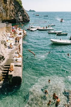 people are swimming in the water near some boats and cliffs, while others swim nearby