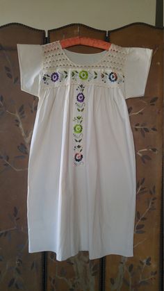 "80s cream cotton boho hippie peasant dress. Embroidered flowers down front panel and across top. Ribbon trim around panel and across top. Crochet neck. Short wide sleeves. Can be worn with a belt or open free style. Arm pit to arm pit 21\" ( up to 42 bust) across middle of dress 30\", length 43\", across shoulders 17\"" White Cotton Peasant Dress For Spring, Spring Peasant Top With Yoke Detail, White Bohemian Peasant Top With Embroidered Hem, Spring Peasant Top With Yoke, White Hippie Peasant Top For Festival, Spring Peasant Dress With Lace Trim, White Bohemian Cotton Peasant Dress, Cream Peasant Top With Floral Embroidery, Summer Embroidered Cream Peasant Top