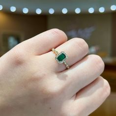 a woman's hand holding a ring with a green stone in it and diamond accents