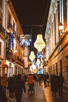 many people are walking down an alley way at night with lights hanging from the buildings