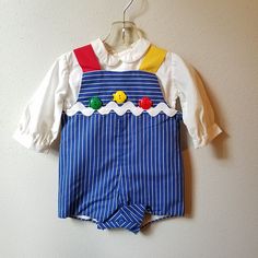 "- This great vintage outfit by C.I. Castro and Co. is perfect for any occasion. The romper is blue and white striped with one red strap and one yellow strap. It is fully lined and buttons at back and snaps between legs. The front is detailed with a giant white rick rack trim and 3 plastic fish buttons. The back has large red buttons. The shirt underneath is white and long sleeved with buttons down back. Size is: 12 months Length: 15\"	in stock	34.65 USD	"	3.50 USD	Clothing > Boys' Clothing > Ba Blue Long Sleeve Jumpsuits And Rompers For Playtime, Playful Fitted Blue Jumpsuits And Rompers, Long Sleeve Cotton Overalls With Buttons, Cotton Overalls With Sleeves And Buttons, Summer Cotton Long Sleeve Overalls, Fitted Cotton Overalls With Buttons, Cotton Long Sleeve Summer Overalls, Playful Blue Cotton Jumpsuits And Rompers, Blue Cotton Playful Jumpsuits And Rompers