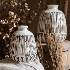 two white vases sitting next to each other on top of a wooden box near dry grass