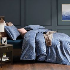 a bed with blue comforter and pillows in a dark room next to a night stand