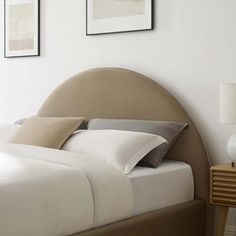 a bed with white sheets and pillows in a bedroom next to two pictures on the wall