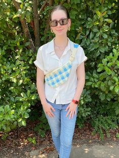 a woman standing in front of bushes with her hands on her hips and wearing sunglasses