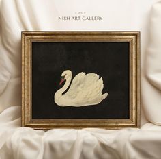 a white swan sitting in front of a black and gold framed art piece with the words hush art gallery on it