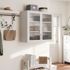 a white cabinet sitting on top of a wooden floor next to a wall mounted coat rack