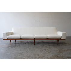 a white couch sitting on top of a cement floor next to a wooden frame wall