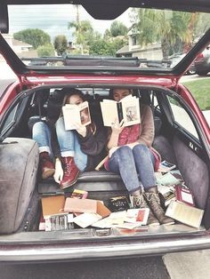 two people sitting in the back of a car reading books