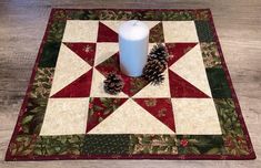 a candle is sitting on top of a quilted placemat with pine cones and holly