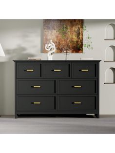 a black dresser with gold handles in a white living room, next to a painting on the wall