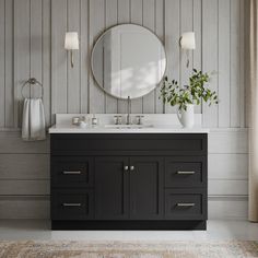 a bathroom vanity with a round mirror above it and two vases on the counter