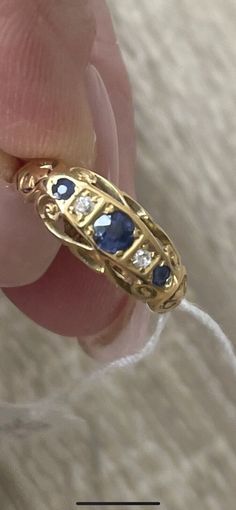 a woman's hand holding a gold ring with blue and white stones on it