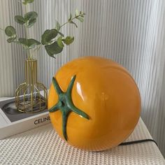 an orange vase with a starfish decoration on it next to a book and plant