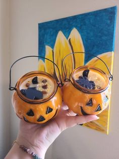 two pumpkin shaped glasses with faces on them are held up in front of a painting