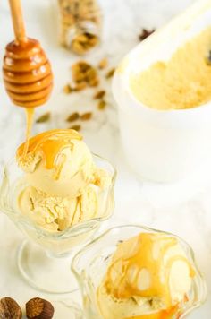 two bowls filled with ice cream and nuts next to a honey dipper on a marble counter