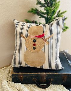 a pillow with a snowman on it sitting next to an old suitcase and christmas tree