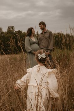 two people standing in tall grass with one person wearing a dress and the other looking at something