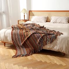 a bed with a blanket on top of it next to a night stand and lamp