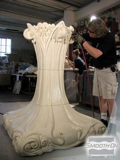 a man working on a large white vase in a room filled with other items and people