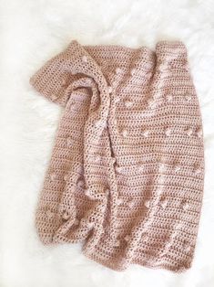 a pink knitted sweater laying on top of a white blanket