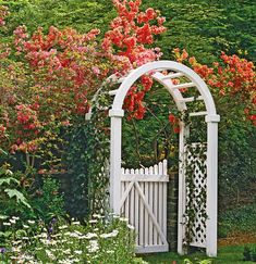 a white garden gate surrounded by trees and flowers