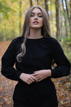 a woman standing in the woods with her hands on her hips and looking off to the side