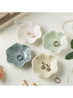 four flower shaped dishes sitting on top of a white table next to pearls and flowers