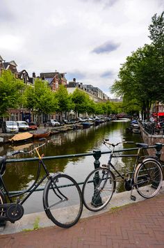 two bikes parked on the side of a bridge over a body of water with boats in the background