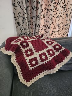 a crocheted blanket sitting on top of a couch next to a window with curtains