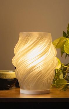 a white vase sitting on top of a wooden table next to a potted plant