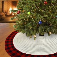 a christmas tree with ornaments on it in front of a fire place and decorated rug