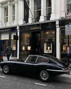 an old black car parked on the side of the road in front of a chanel store