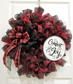 a red and black wreath hanging on a door with the word comfort & joy written on it