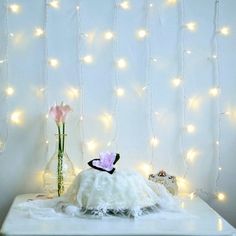 a white table topped with a vase filled with flowers next to a wall covered in fairy lights