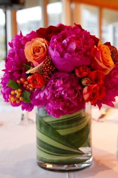 a vase filled with lots of colorful flowers on top of a white tablecloth covered table