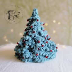 a crocheted blue christmas tree with red balls on it's base and a white background