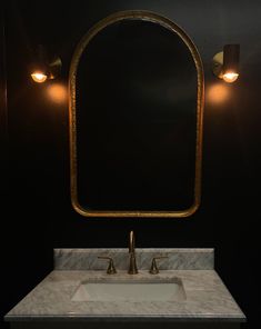 a bathroom sink under a large mirror with lights on it's sides and an oval gold framed mirror above it